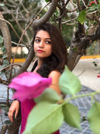 Young woman looking away while standing by tree at park