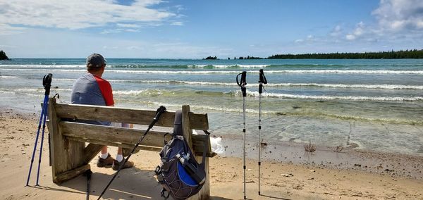 Rear view of man sitting on beach at beach against sky