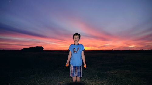 Boy holding lit candles while standing on grassy field at dusk