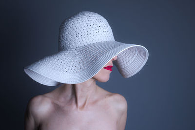 Close-up of young woman wearing hat against black background