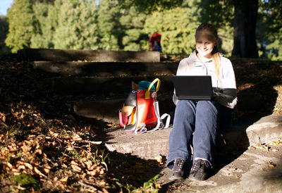 Happy woman using laptop while sitting on steps at park