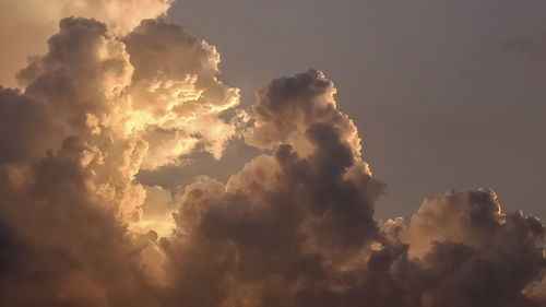 Low angle view of sunlight streaming through clouds during sunset