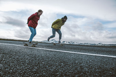 Full length of couple skateboarding on road against sky