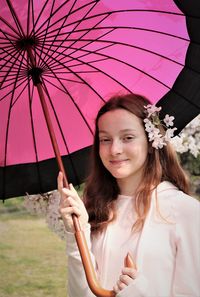 Portrait of young woman holding pink while standing against plants