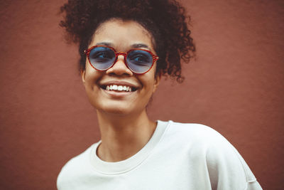 Smiling teenage girl wearing eyeglasses standing against wall