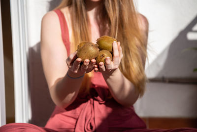 Midsection of young woman holding kiwis against wall