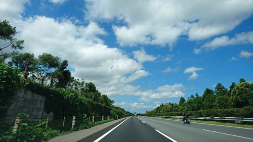 Road amidst trees against cloudy blue sky