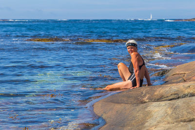 Portrait of woman sitting on rock at sea against sky