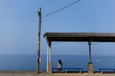 Rear view of woman sitting on bench against sea and sky