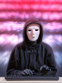 Portrait of woman wearing mask while typing on keyboard against blurred background