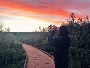 Rear view of man photographing against sky at sunset