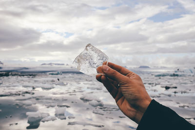 Close-up of hand holding ice against cloudy sky