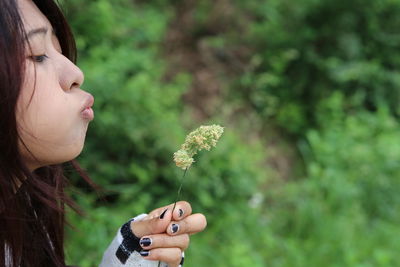 Side view of woman blowing flower in park