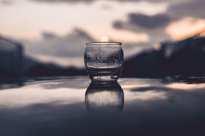 Close-up of water in glass on table against sky during sunset