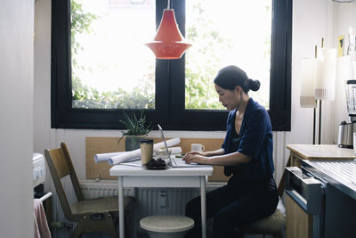 Side view of female architect using laptop at desk in home office