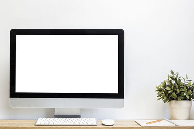 A mock up computer device with notebook on table with white wall.