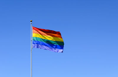 Low angle view of rainbow flag against clear blue sky