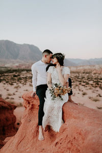 Young couple standing on rock against sky