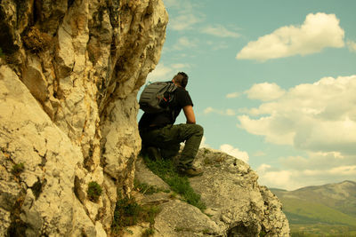 Man siting by rock formation against sky