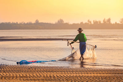 Rear view of man fishing in sea against clear sky during sunset