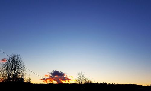 Silhouette trees on field against clear sky