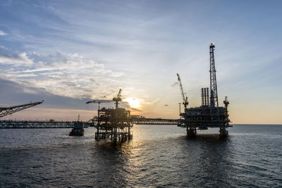 Cranes at commercial dock against sky during sunset