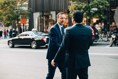 Mature businessman greeting male colleague on street in city