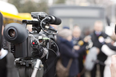 Close-up of television camera with people in background