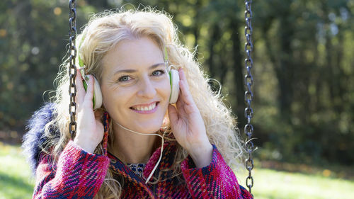 Portrait of smiling woman wearing headphones while sitting on swing 