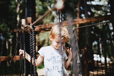 Girl child playing on a rope in the outdoor playground, adventure park.