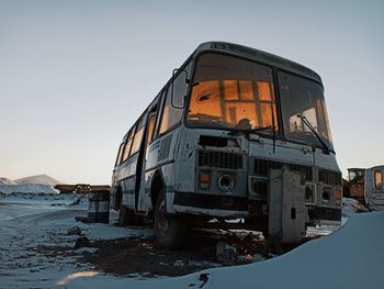 Abandoned vehicle on field against clear sky during sunset