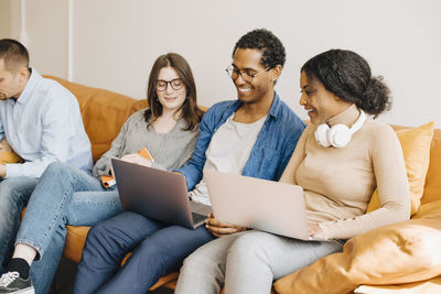 Smiling programmers working over laptops while sitting on sofa in creative office