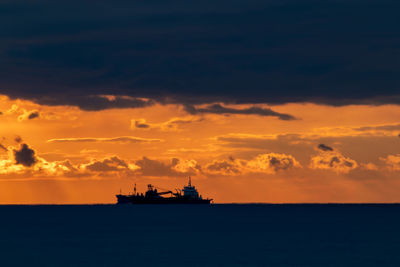 Silhouette ship in sea against sky during sunrise.
