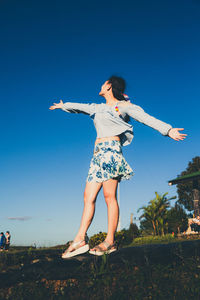 Woman with arms outstretched standing on grass against blue sky