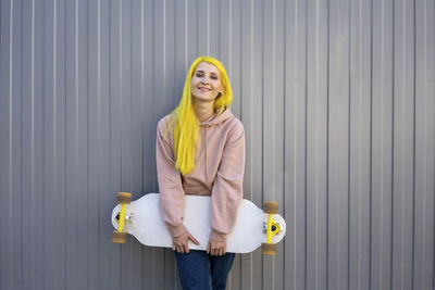 Portrait of a smiling young woman standing against wall