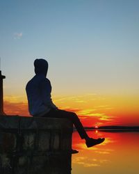 Rear view of silhouette man sitting against sky during sunset