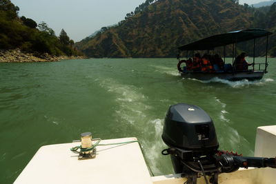 People sitting on boat in river against mountains