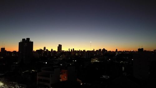Silhouette buildings in city against clear sky at night