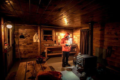 A man stands in a cold cabin waiting for the fire to warm up