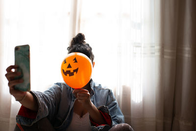 Close-up of woman holding halloween decoration against face and taking selfie at home