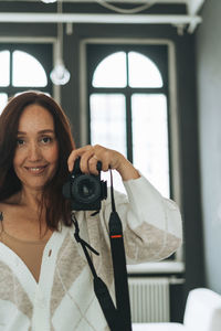 Portrait of young woman photographing through window