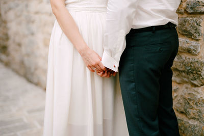 Midsection of couple holding hands while standing outdoors