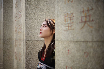 Portrait of a young woman looking away against wall