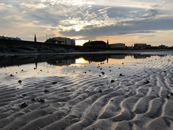 Buildings by beach against sky during sunset