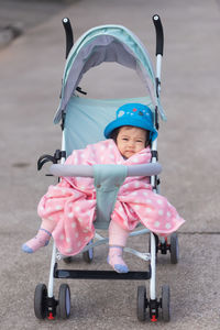 Portrait of cute baby wearing hat sitting on baby stroller outdoors