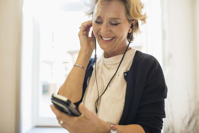 Smiling businesswoman listening to music through mobile phone in office