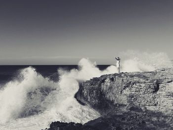 Waves breaking against sea against clear sky