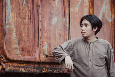 Portrait of young man looking away against wall