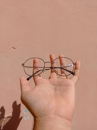 Close-up of hand holding eyeglasses against wall