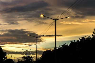 Low angle view of illuminated street light and silhouette tree against sky during sunset 